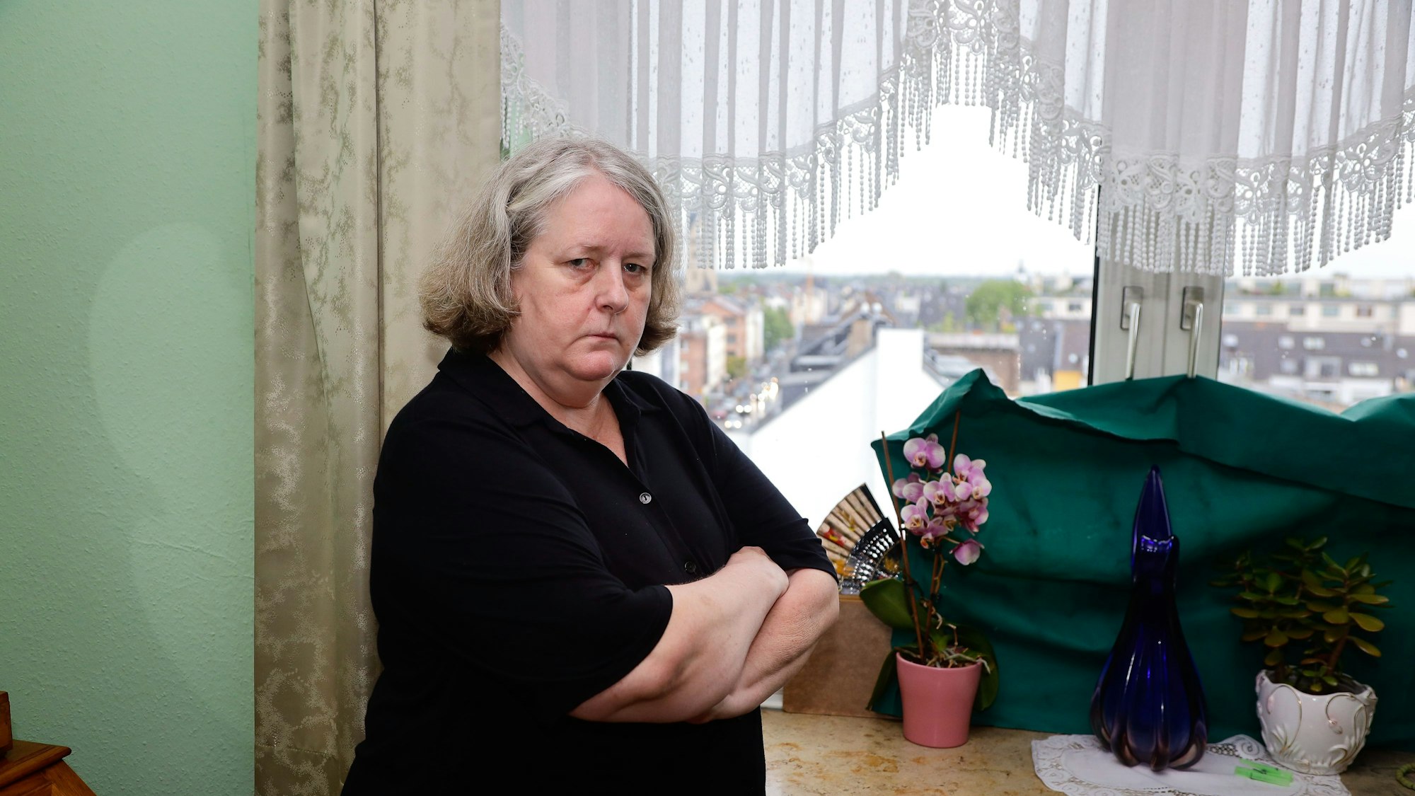 Hildegart Scholten (Name geändert) steht mit verschränkten Armen vor dem Fenster ihrer Wohnung. Sie wird permanent von Geräuschen eines Funkmastes auf dem Dach ihrer Wohnung gestört.