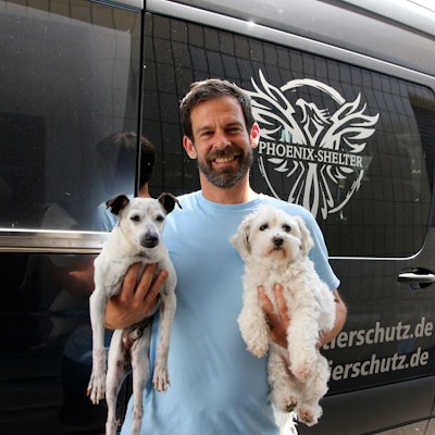 Marcel Tong strahlt in die Kamera, in jedem Arm hält er einen Hund mit hellem Fell.