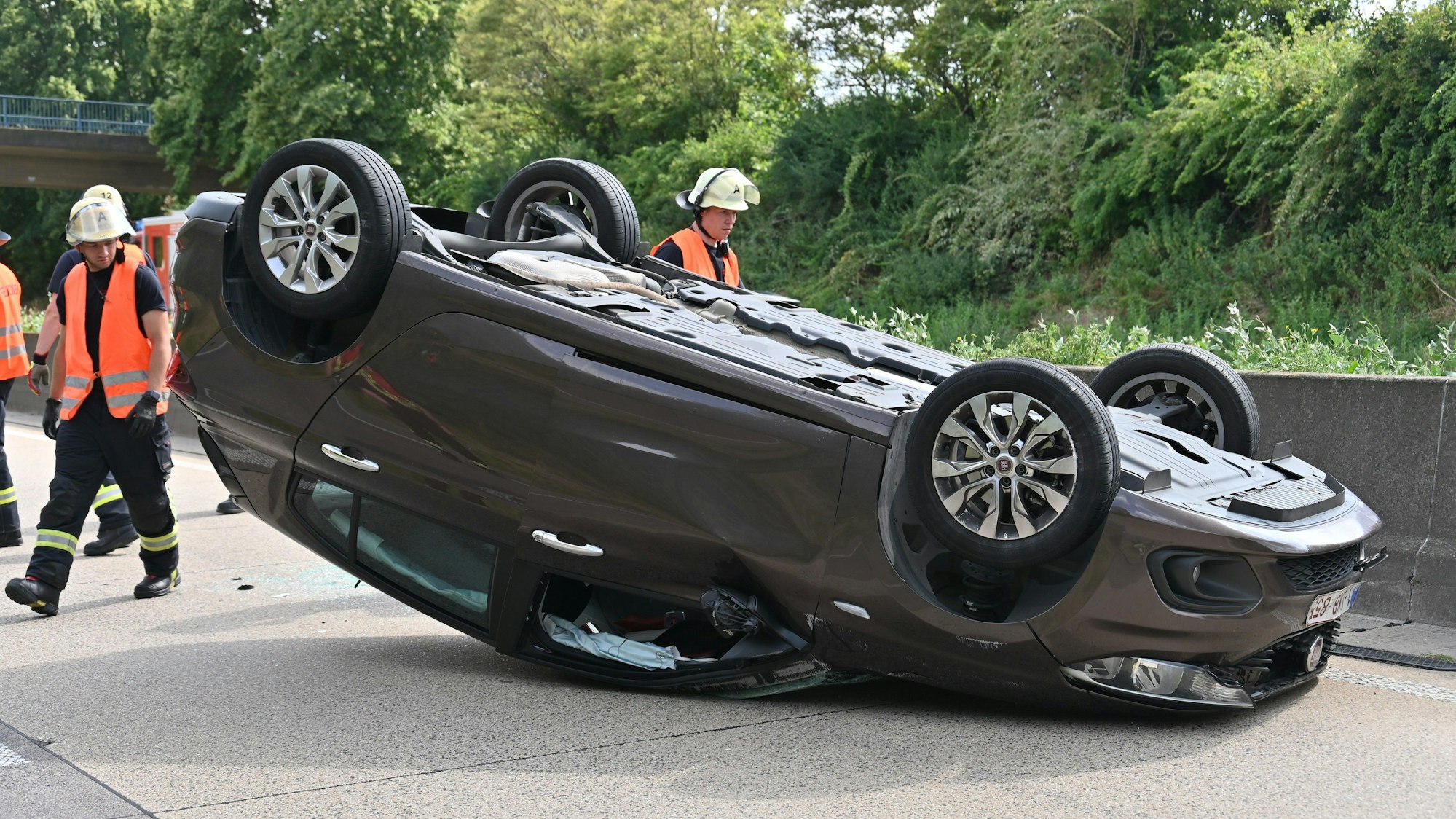 Das Bild zeigt einen auf dem Dach liegenden Wagen und mehrere Rettungskräfte auf der Fahrbahn.