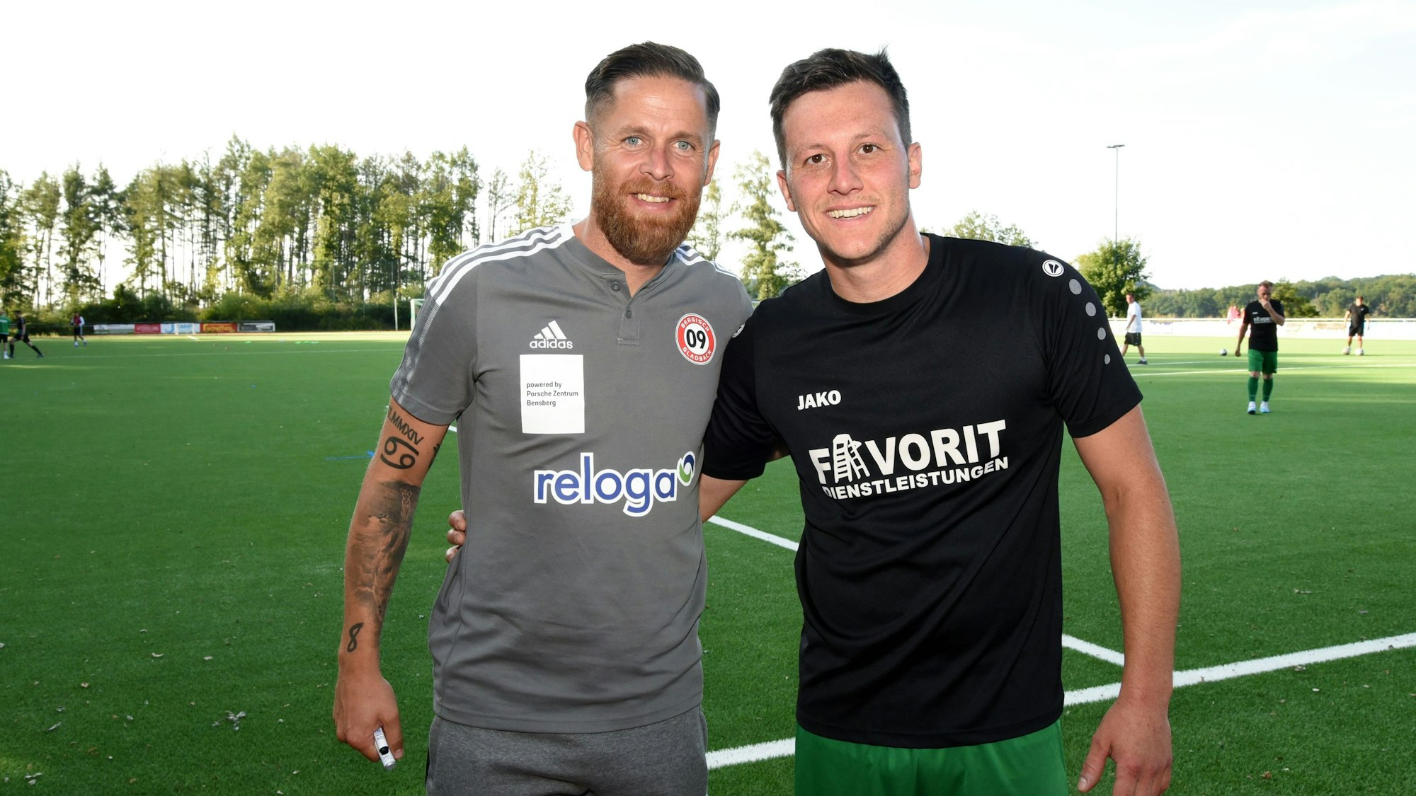 Zwei Fußballtrainer stehen am Spielfeldrand.