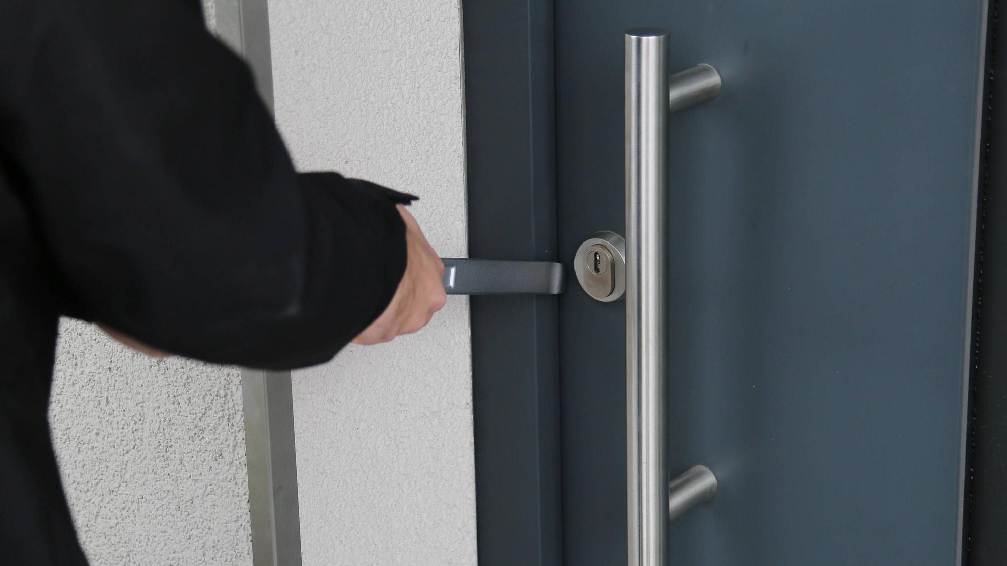 Ein Einbrecher öffnet eine Tür mit einem Brecheisen.