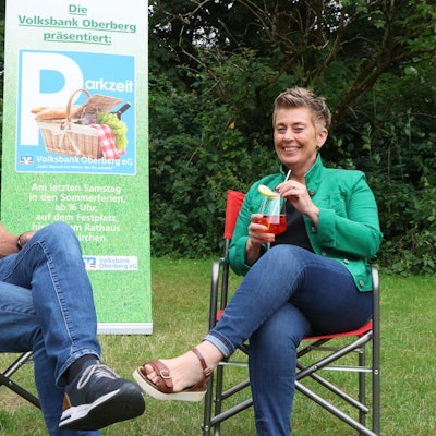 Ein Mann und eine Frau sitzen in Campingstühlen auf der Wiese und trinken Cocktails.