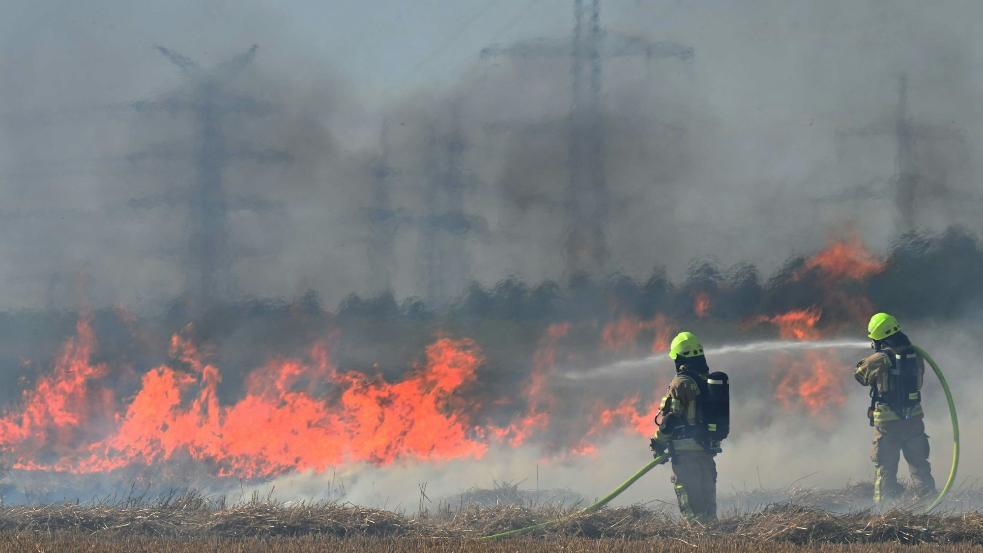Das Bild zeigt zwei Feuerwehrmänner an einem brennenden Stoppelfeld