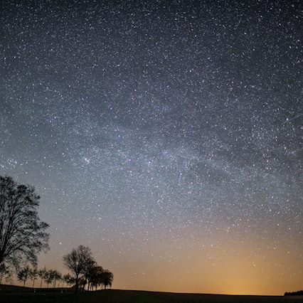Der Sternenhimmel leuchtet in der Nacht über der Landschaft.