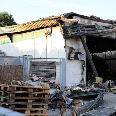 Vor dem abgebrannten Lager stehen Paletten.