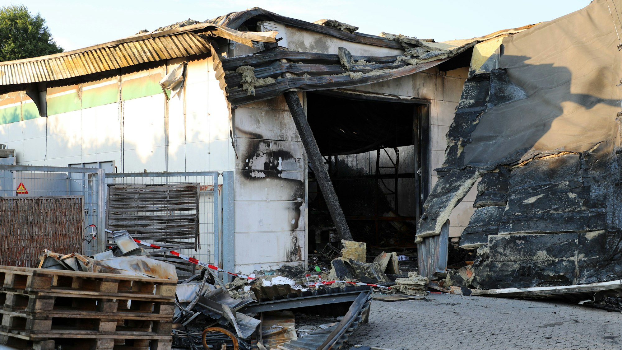 Vor dem abgebrannten Lager stehen Paletten.