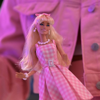 Barbie-Puppe vor einer rosa Jeansjacke mit Barbie-Logo