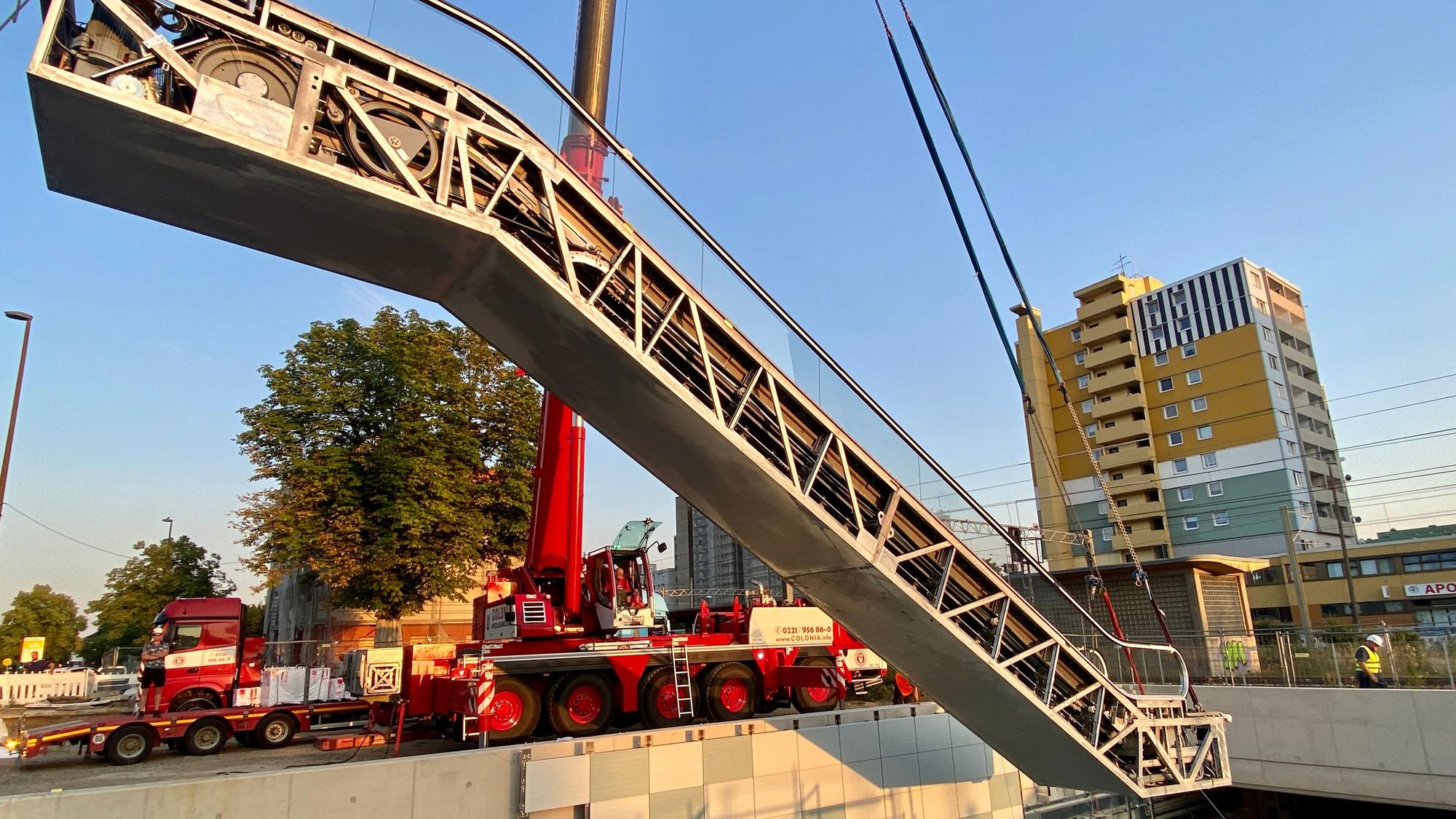 Eine Rolltreppe wird an einem Kran in eine Unterführung gehoben.