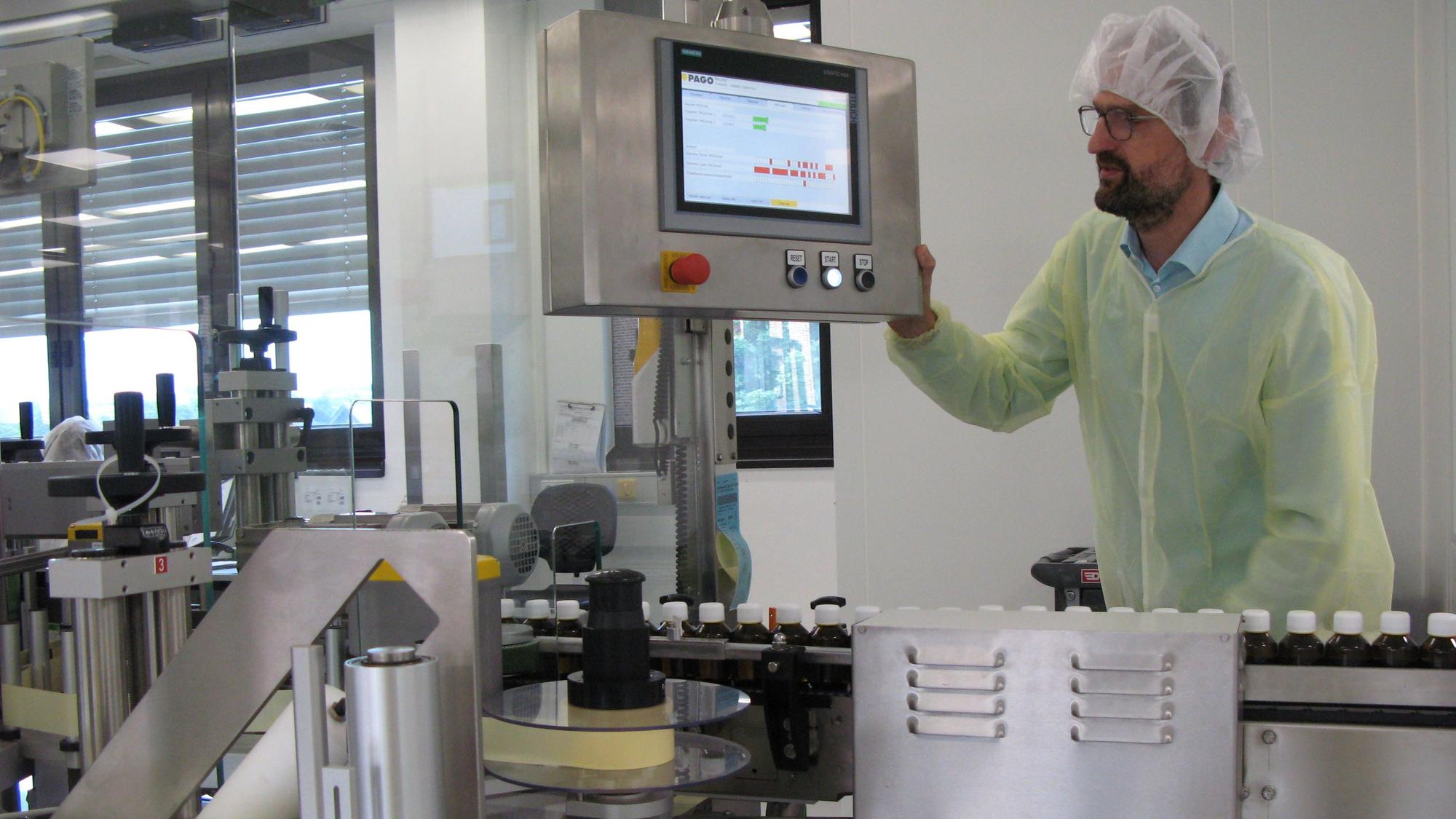 Ein Mann in Schutzkleidung und Haarhaube bedient eine moderne Verpackungsanlage mit Computerbildschirm.