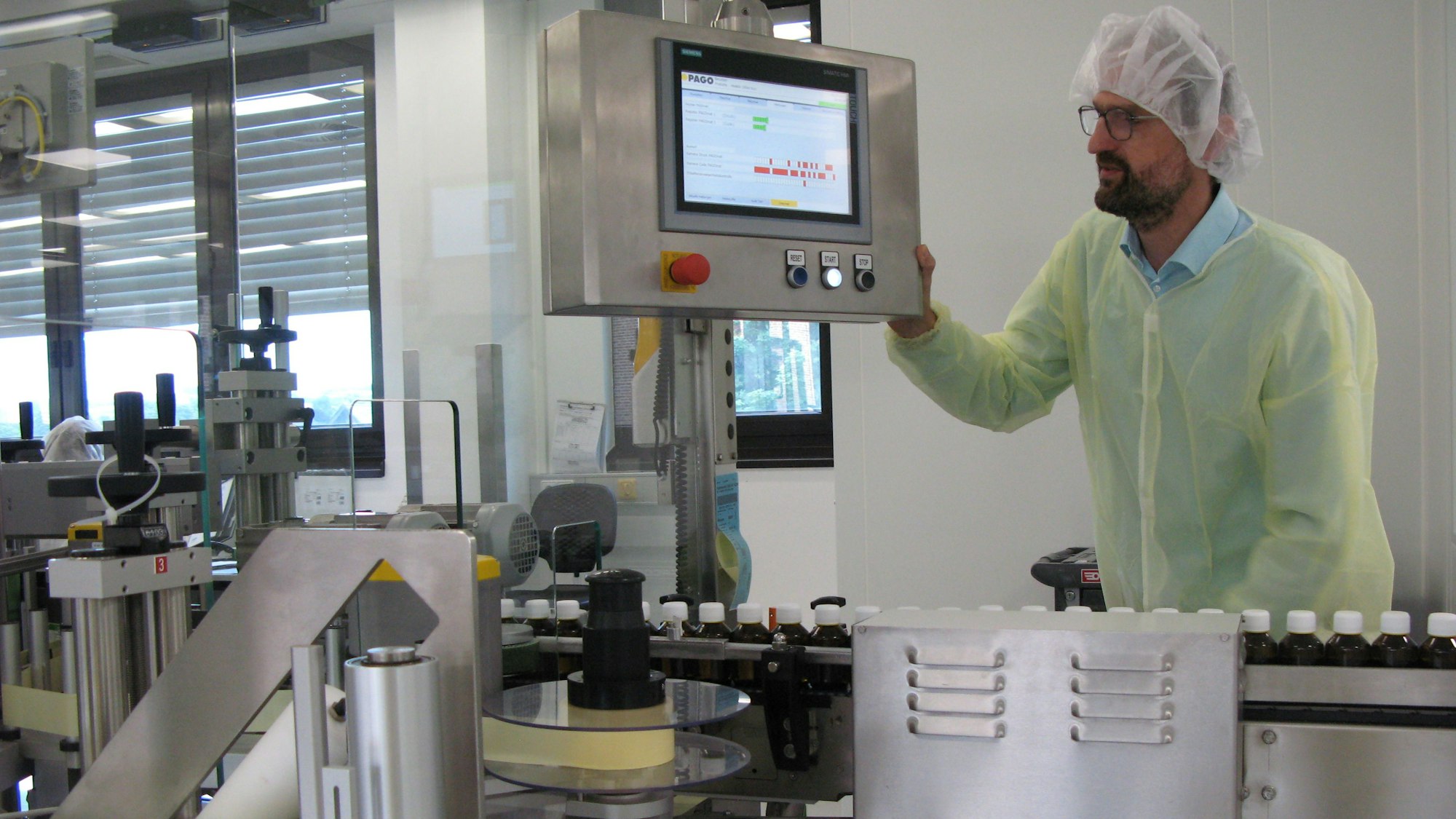 Ein Mann in Schutzkleidung und Haarhaube bedient eine moderne Verpackungsanlage mit Computerbildschirm.