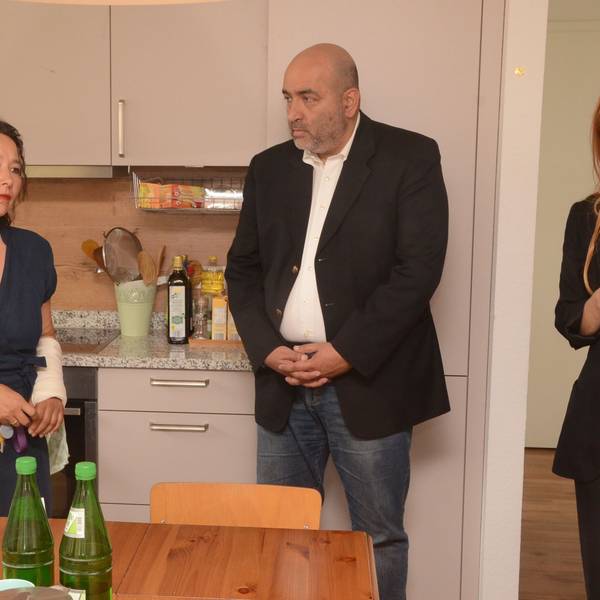 Eine Frau und ein Mann stehen in der Küche des Frauenhauses. Die Frau berichtet dem Mann von ihrer Arbeit.