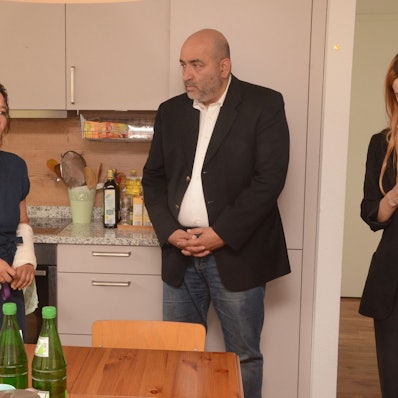 Eine Frau und ein Mann stehen in der Küche des Frauenhauses. Die Frau berichtet dem Mann von ihrer Arbeit.