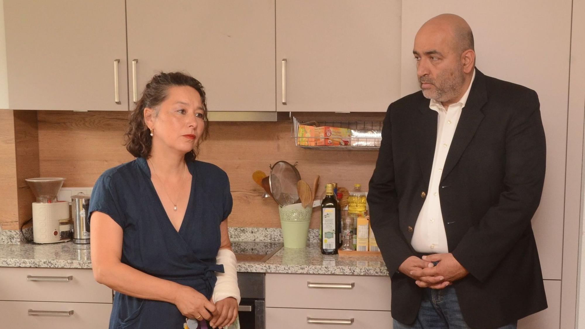 Eine Frau und ein Mann stehen in der Küche des Frauenhauses. Die Frau berichtet dem Mann von ihrer Arbeit.