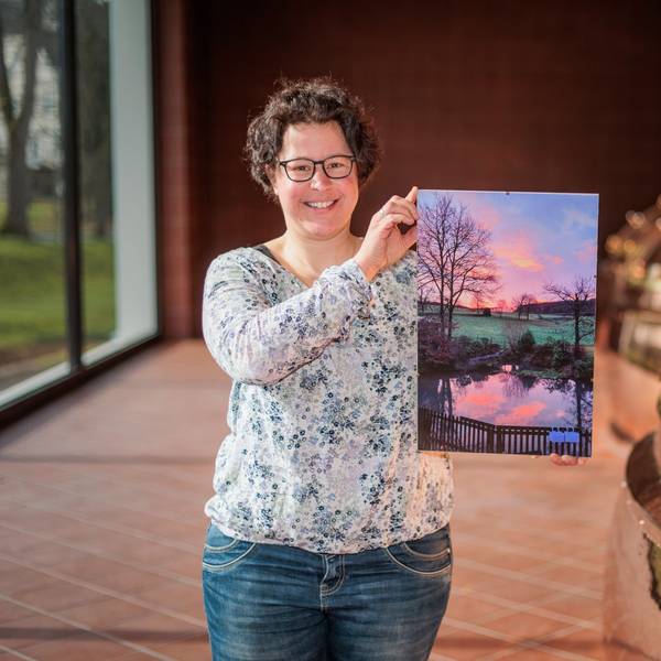 Eine Frau hält ein Foto eines Teiches im Sonnenaufgang in den Händen.