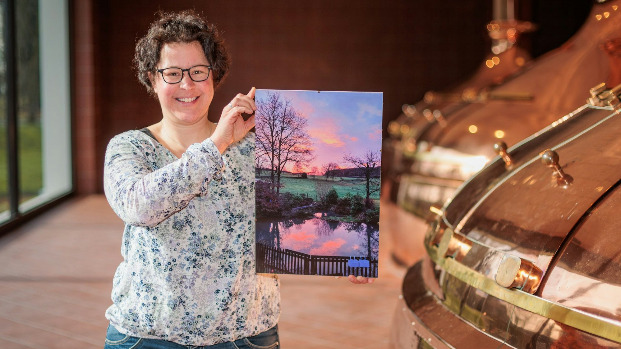 Eine Frau hält ein Foto eines Teiches im Sonnenaufgang in den Händen.
