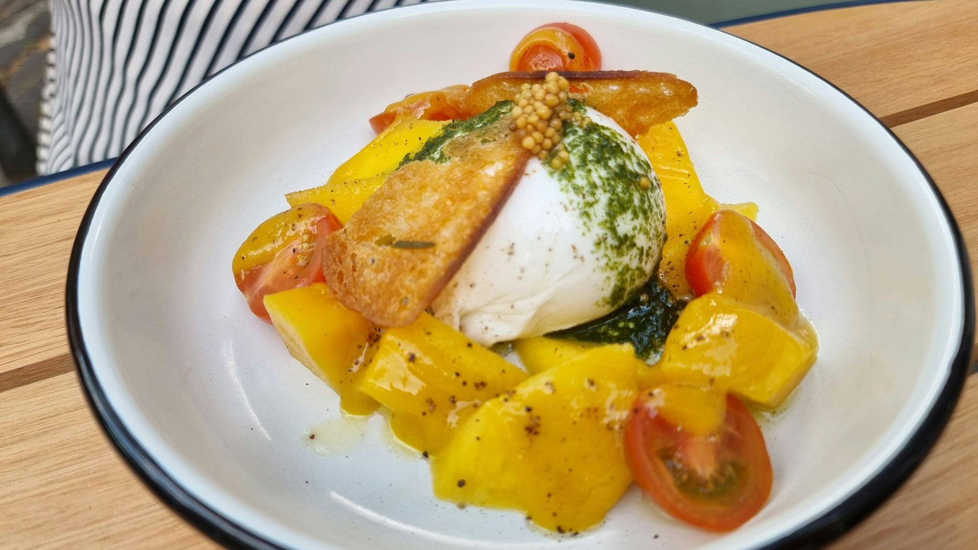 Burrata mit Mango, ein paar Kirschtomaten und Basilikum-Pesto, angerichtet auf einem Teller