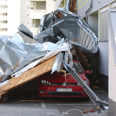 Teile eines von starken Sturmböen abgedeckten Dachs liegen auf Fahrzeuge, die auf einem Parkplatz abgestellt sind.