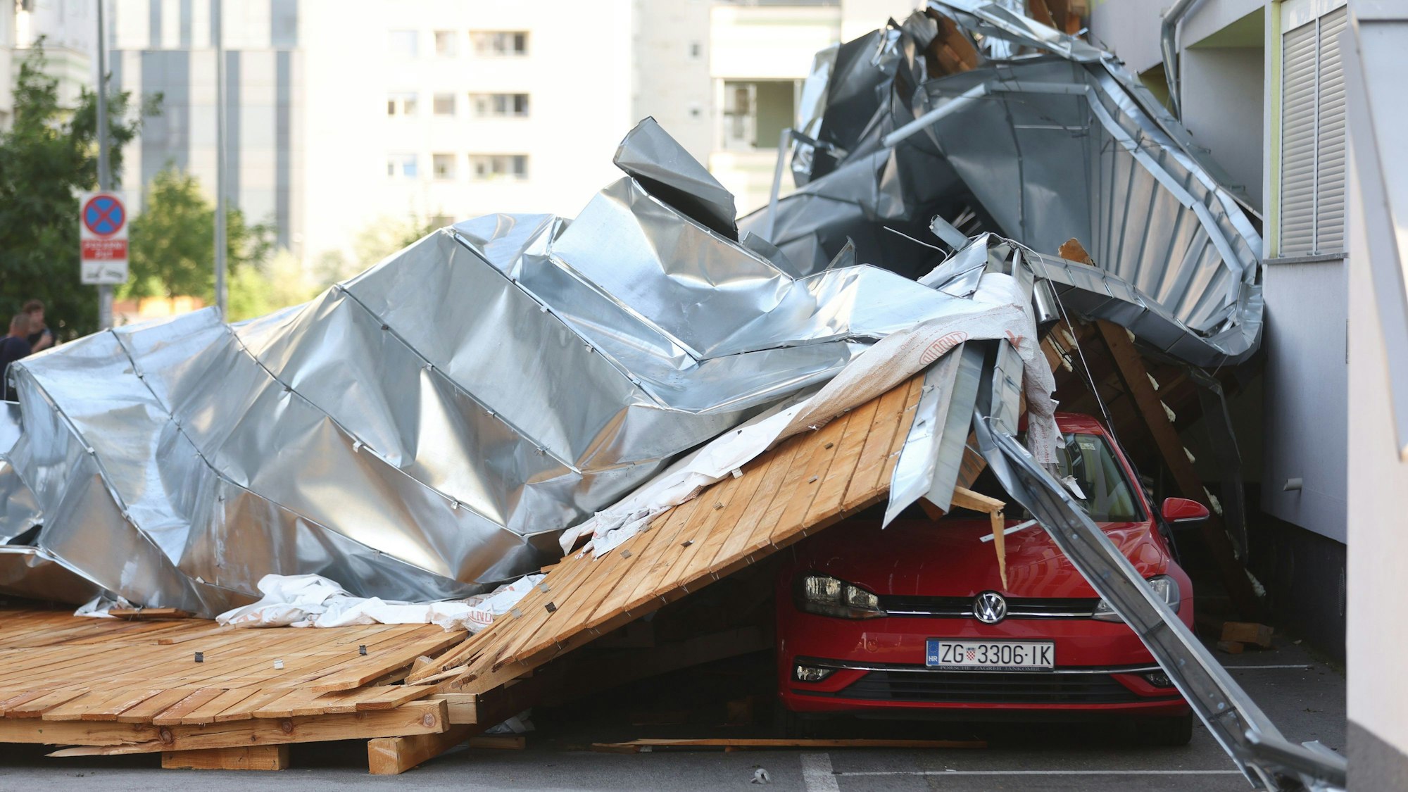 Teile eines von starken Sturmböen abgedeckten Dachs liegen auf Fahrzeuge, die auf einem Parkplatz abgestellt sind.