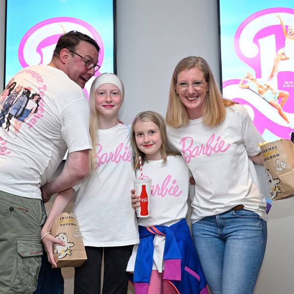 Familie Sauer steht vor Barbie-Plakaten.