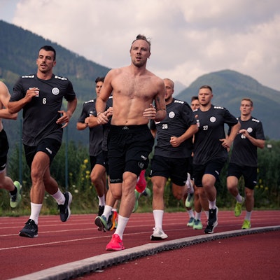 Eine Gruppe von Männern läuft, im Hintergrund die Alpen.