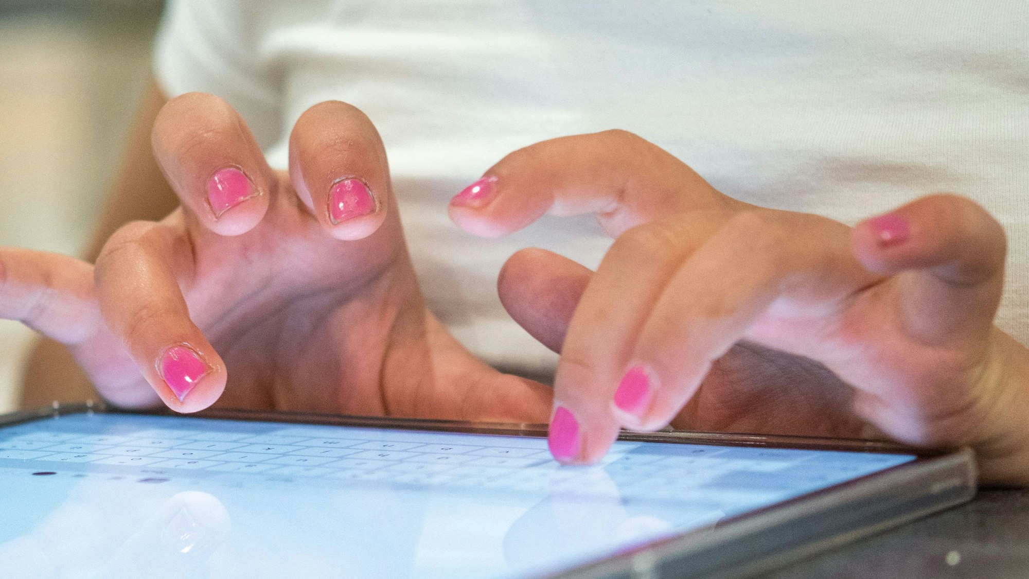Eine Grundschülerin sitzt an einem Tabletcomputer und tippt.