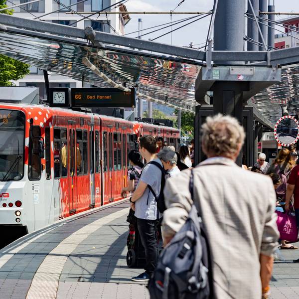 Eine rot-weiße Straßenbahn an einer Haltestelle. Menschen warten auf den Zug.