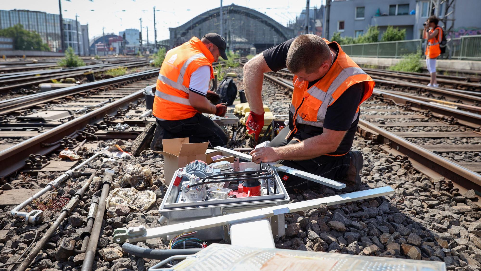 Zwei Männer in Warnwesten schrauben an den Gleisen am Kölner Hauptbahnhof.