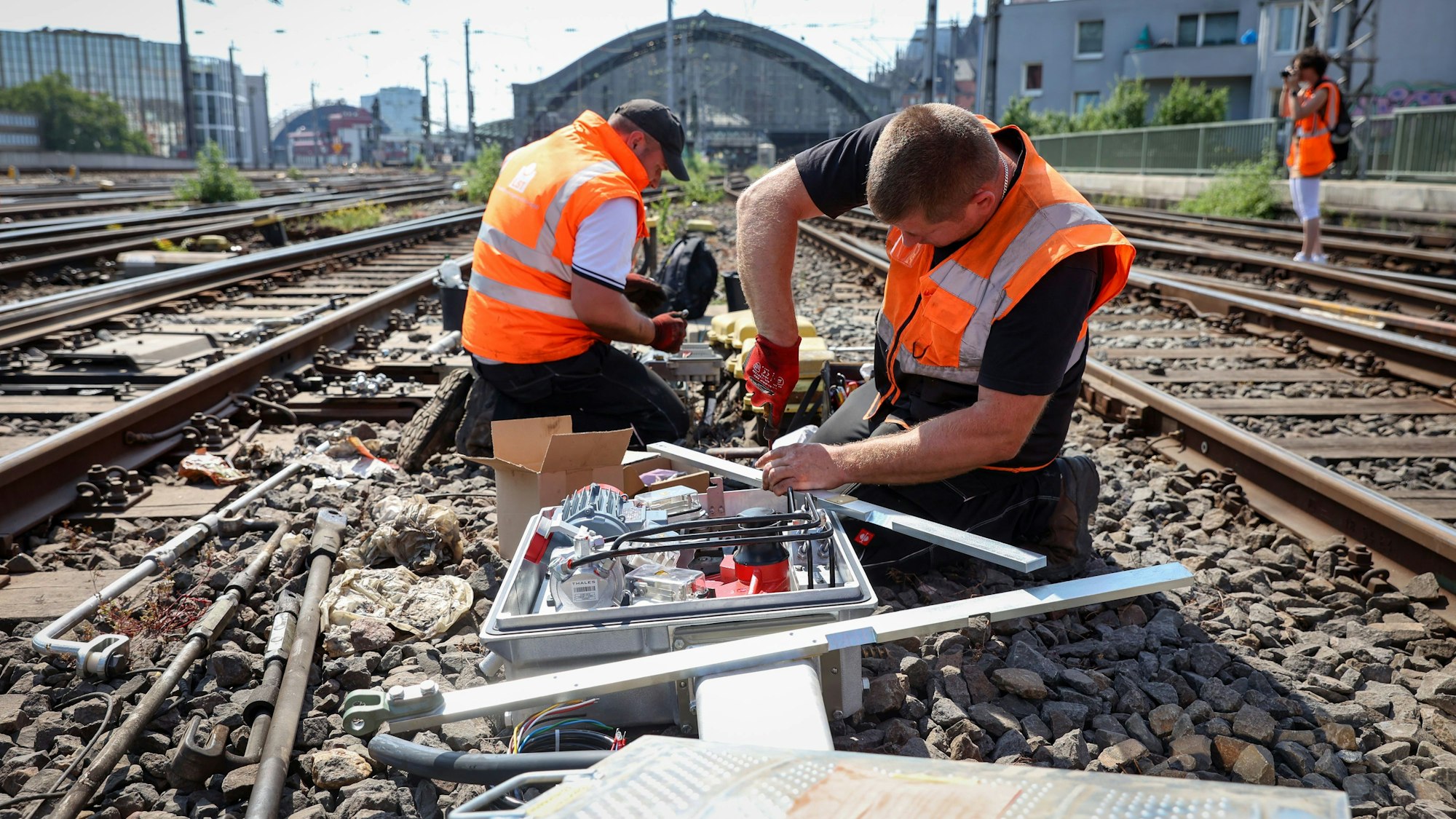 Zwei Männer in Warnwesten schrauben an den Gleisen am Kölner Hauptbahnhof.