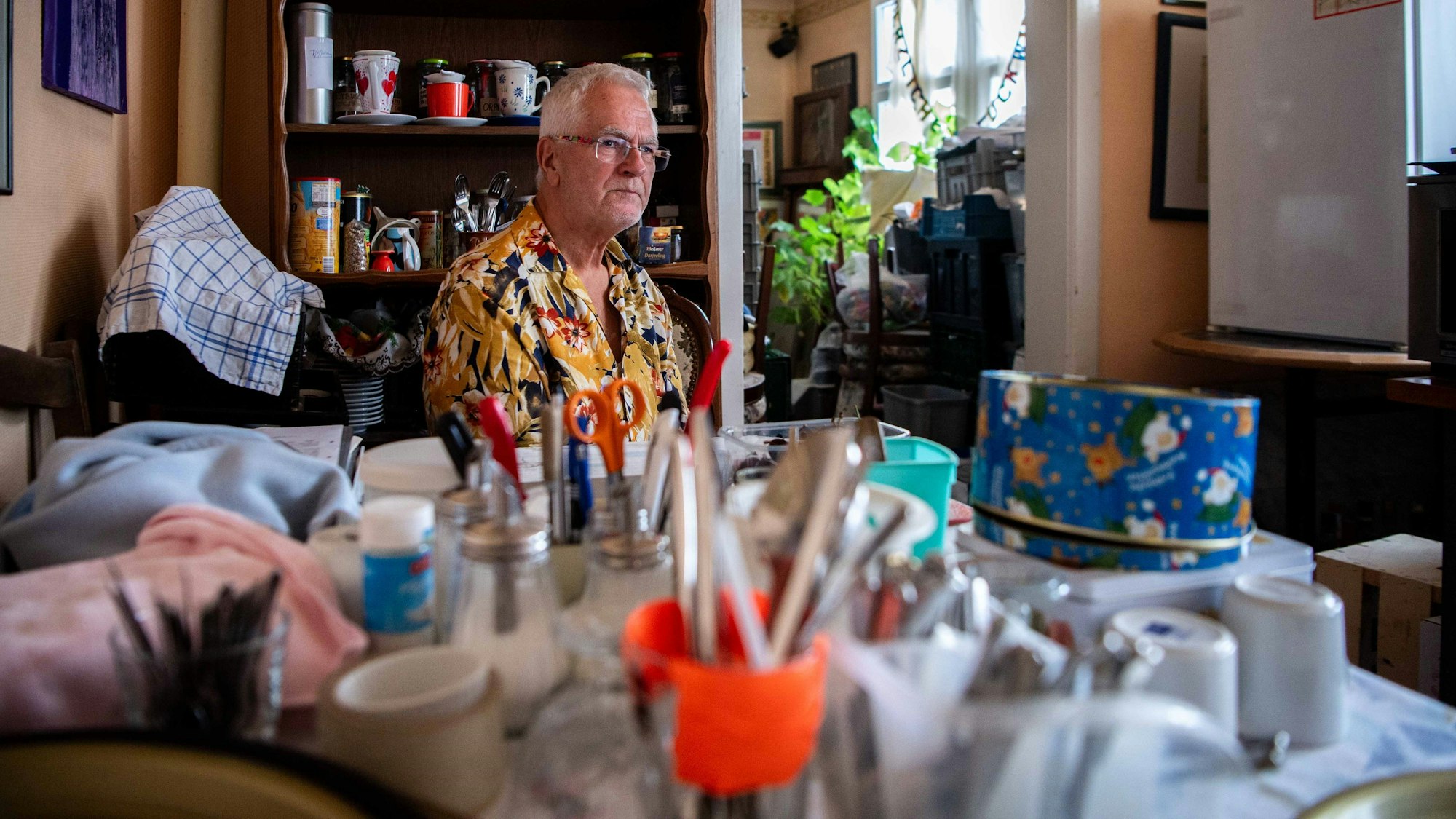 Ein Mann sitzt an einem Tisch. Darauf sind unscharf zahlreiche Dinge zu sehen, die er nach der Flut aus seinem Café gerettet hat.