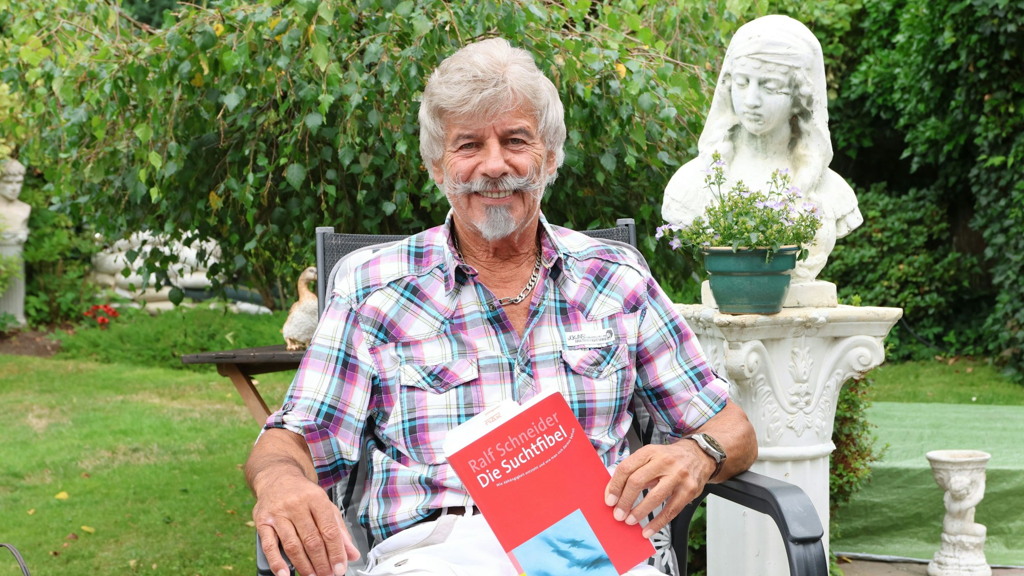 Ein Mann sitzt mit einem Buch über Suchtkrankheiten in der Hand im Garten.