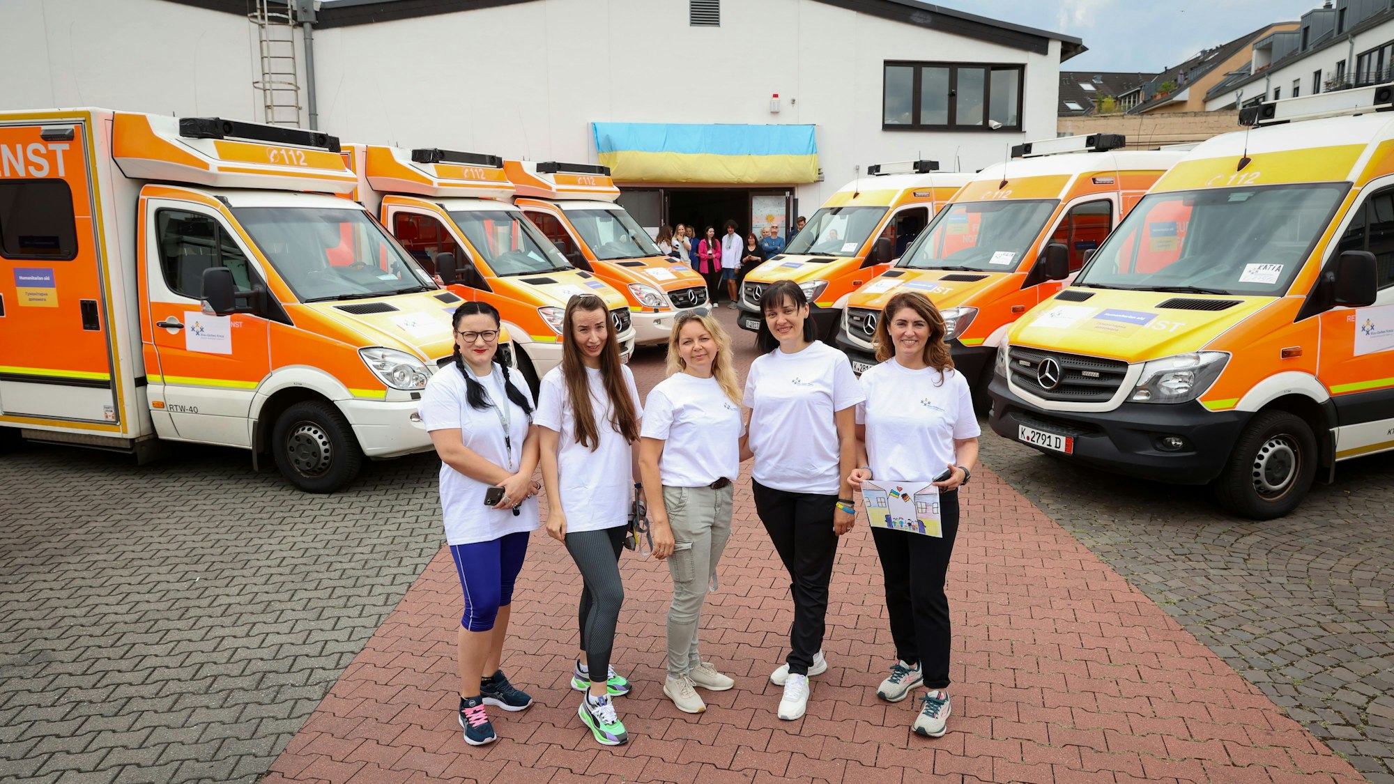 Fünf Frauen stehen vor gespendeten Fahrzeugen für Ukraine.