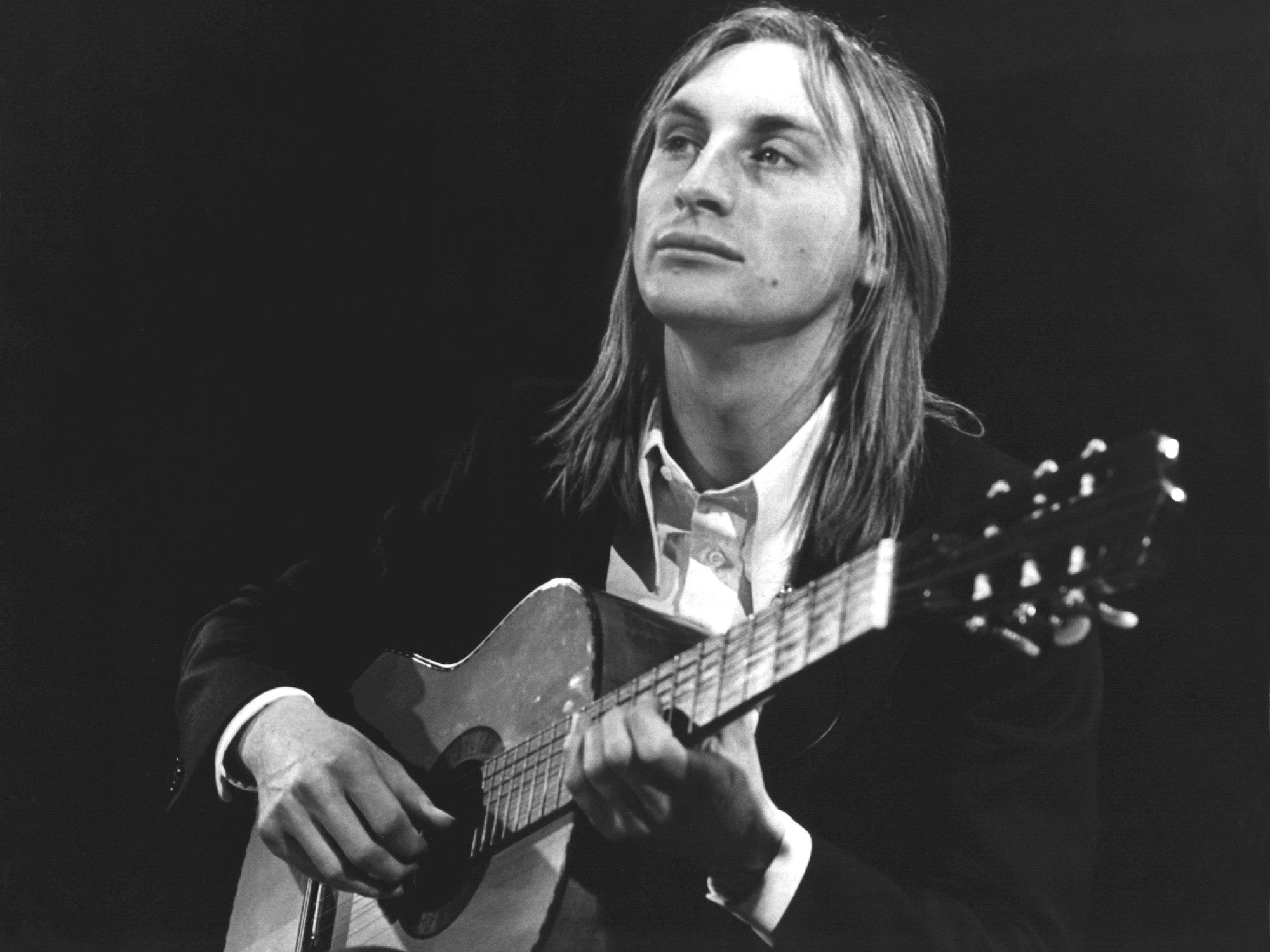 Otto Waalkes sitzt als junger Mann auf einer Bühne und spielt Gitarre.