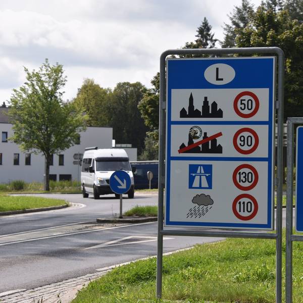 Das Grenzschild von Luxemburg, eingefasst von Europa-Sternen auf blauem Grund, aufgenommen an der deutsch-luxemburgischen Grenze neben einem Schild mit Geschwindigkeitsbegrenzungen.