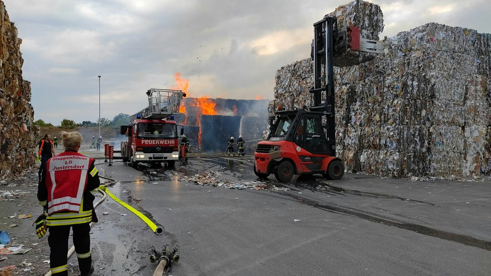 Während die Feuerwehr löscht, werden mit einem Gabelstapler Papierballen weggefahren.