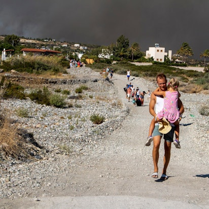 Ein Mann trägt ein Kind, als sie ein Gebiet verlassen, in dem ein Waldbrand auf der griechischen Insel Rhodos wütet. Ein großes Waldfeuer hat die Behörden gezwungen, die Evakuierung von vier Orten anzuordnen, darunter zwei Badeorte.