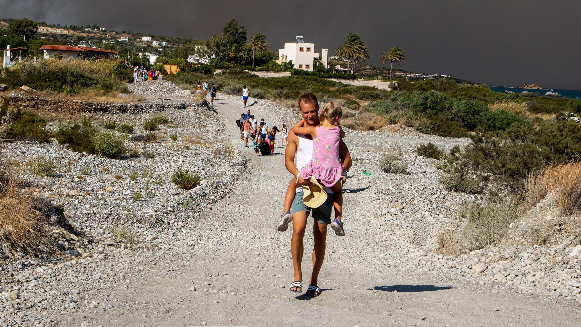Ein Mann trägt ein Kind, als sie ein Gebiet verlassen, in dem ein Waldbrand auf der griechischen Insel Rhodos wütet. Durch den vom Menschen gemachten Klimawandel könnten derartige Szenen in Zukunft häufiger werden.