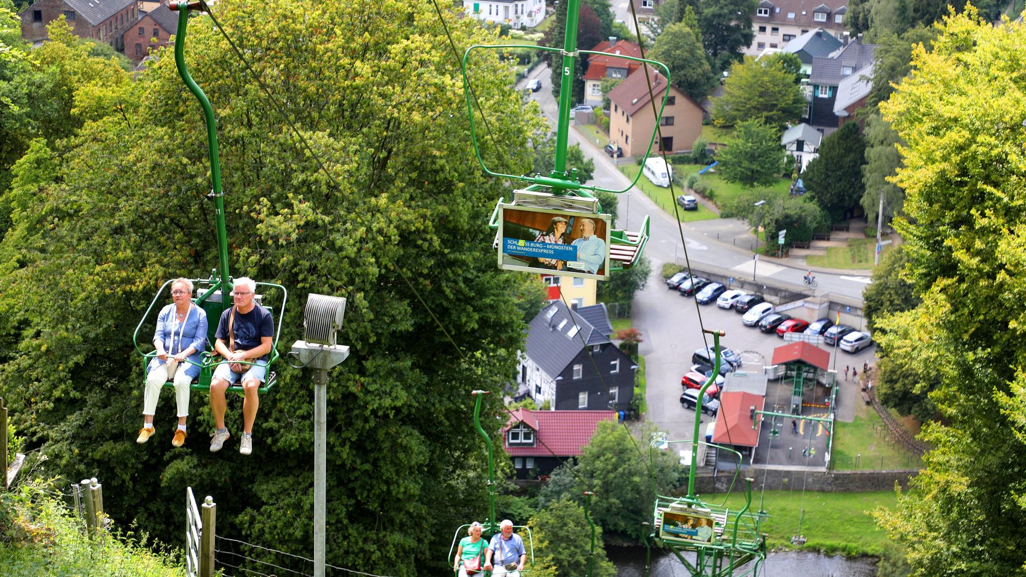 Blick ins Tal: Menschen fahren mit einem Sessellift von der Talstation am Ufer der Wupper den Berg hinauf.