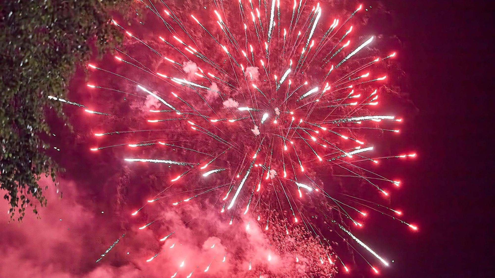 Ein roter Funkenregen explodierender Feuerwerksraketen erleuchtet den Nachthimmel.