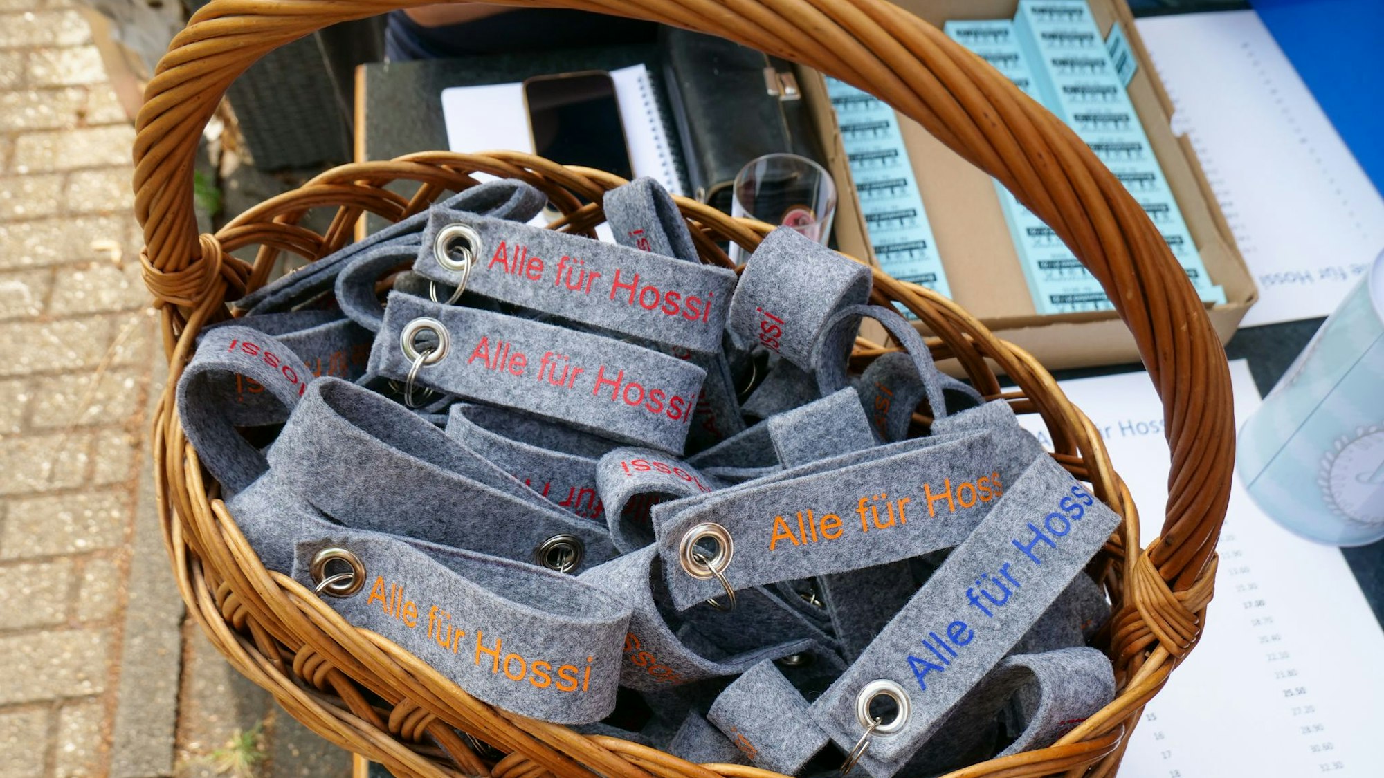 Auf dem Foto ist ein Korb mit handgefertigten Schlüsselanhängern zu sehen. Darauf ist zu lesen„ Alle für Hossi“.