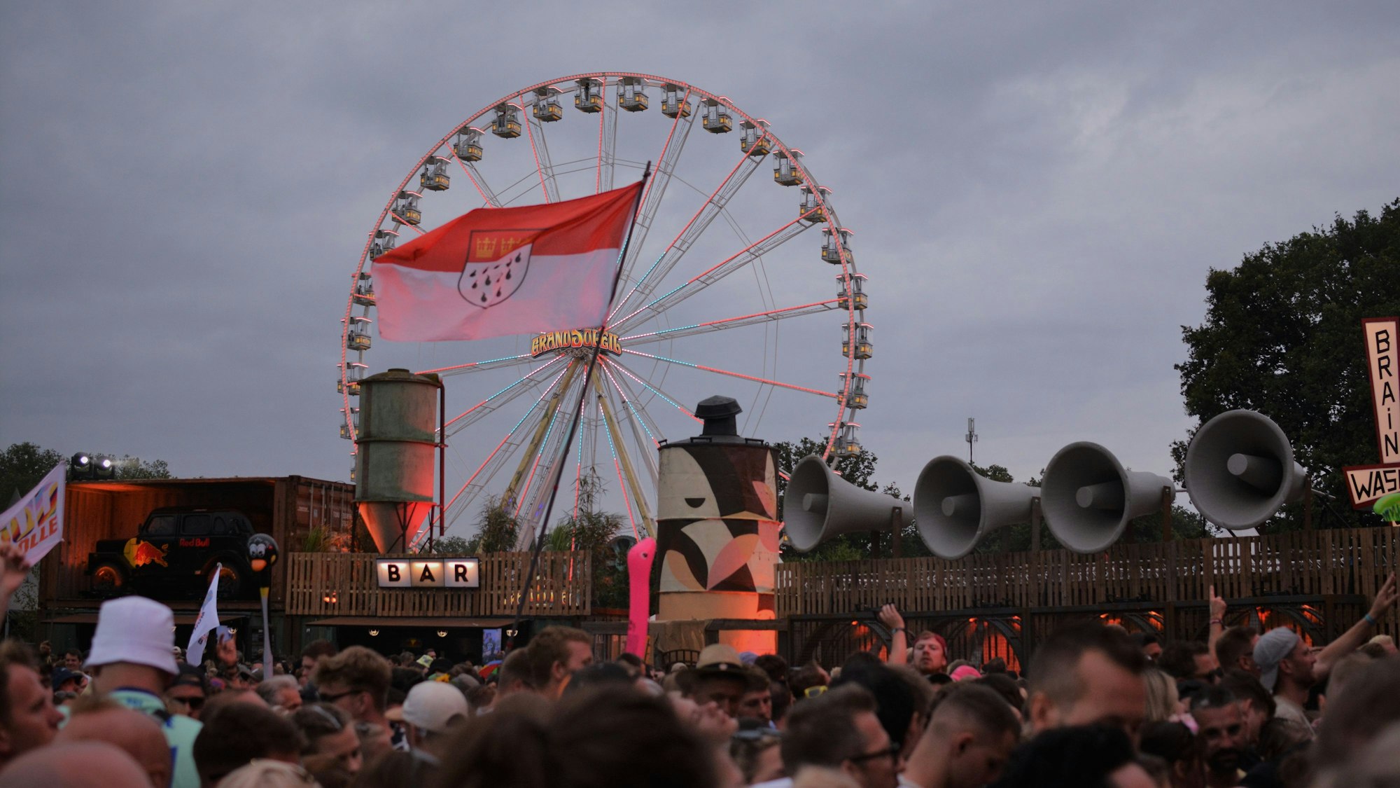 Eine Kölner Fahne weht, im Hintergrund das Riesenrad von Parookaville.