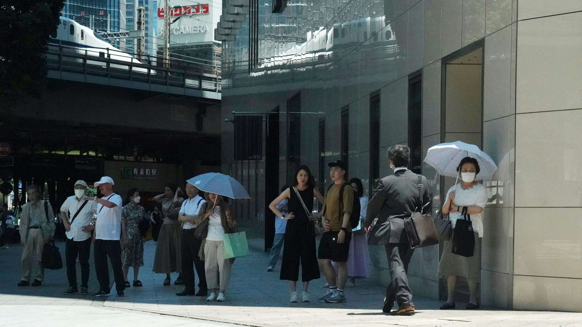 12.07.2023, Japan, Tokio: Menschen warten bei einer Ampel im Schatten, bis sie eine Straße überqueren können.