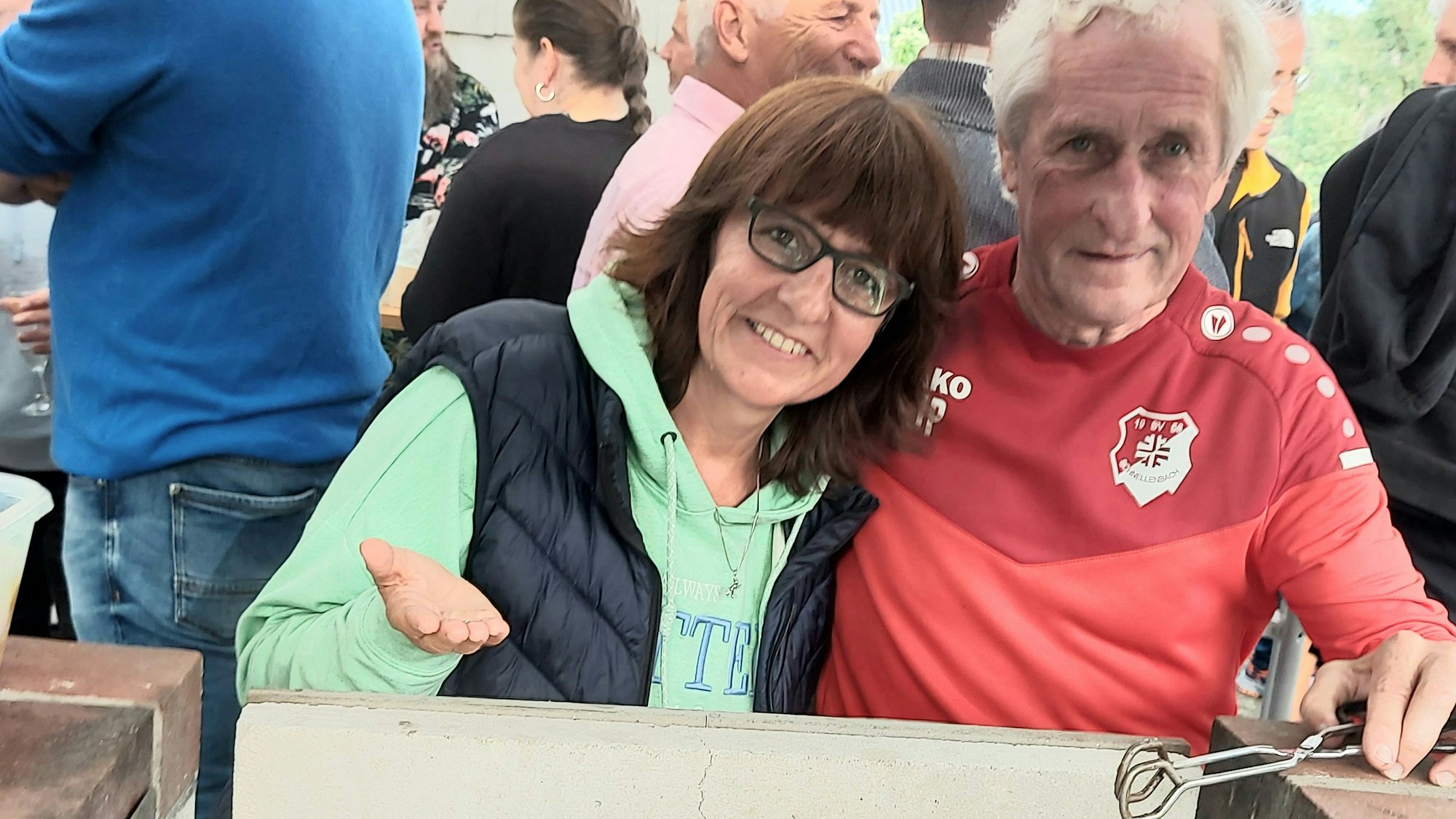 Eine Frau und ein Mann stehen an einem Grill nebeneinander.