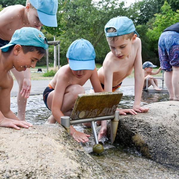 Kinder mit Mützen spielen an einem Flusslauf.