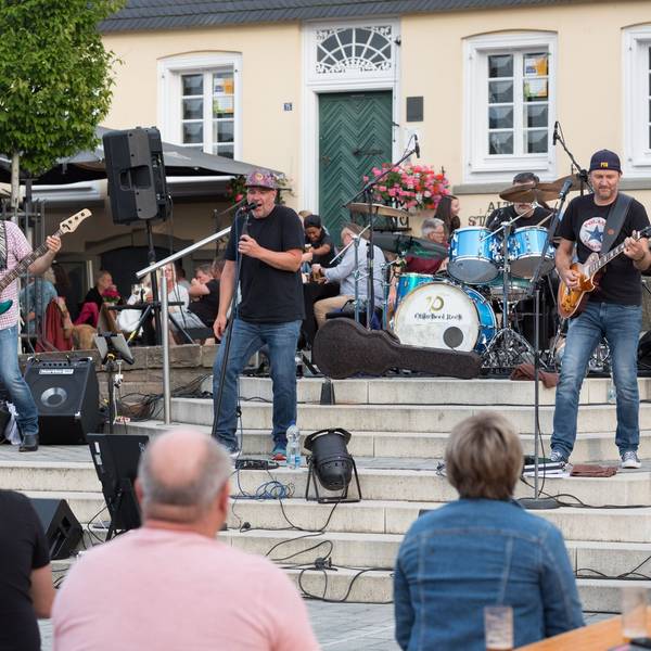 Eine Band spielt auf Treppen in einem Stadtzentrum vor Publikum.