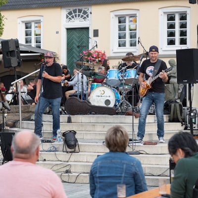 Eine Band spielt auf Treppen in einem Stadtzentrum vor Publikum.