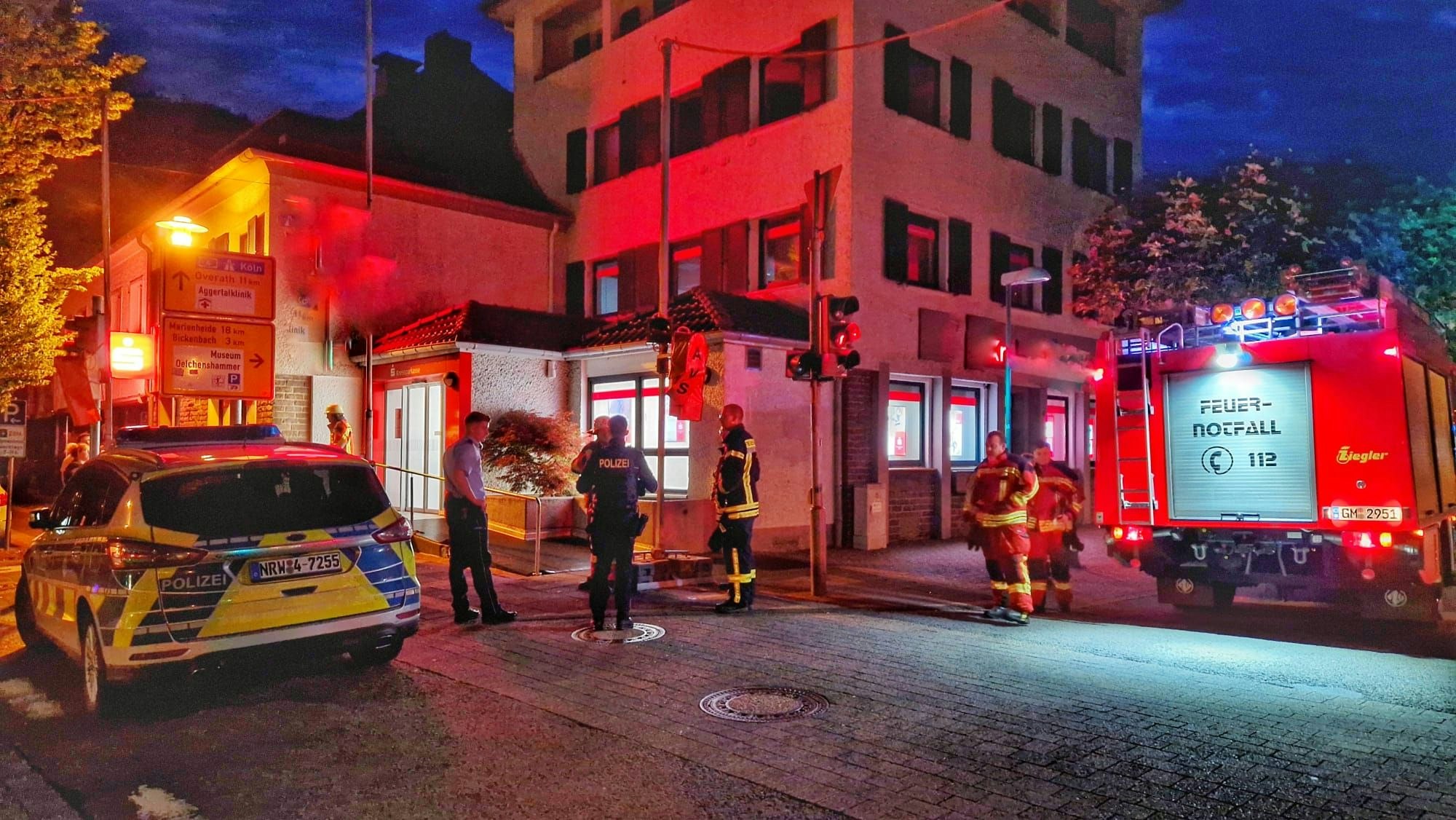 Ein Feuerwehr- und Polizeiauto stehen vor einer Bankfiliale im Dunkeln.