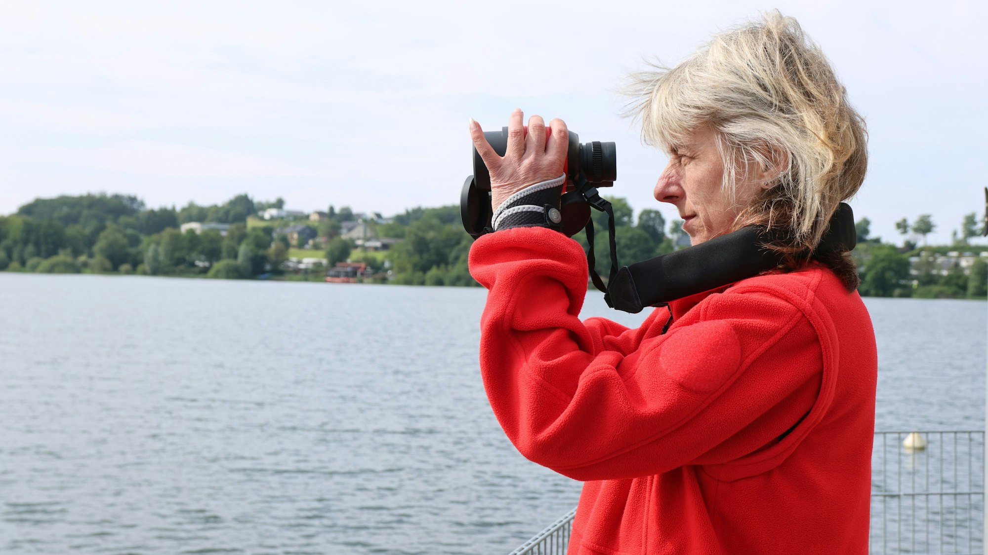 Eine Frau in rotem Fließpullover schaut durch ein Fernglas aufs Wasser.