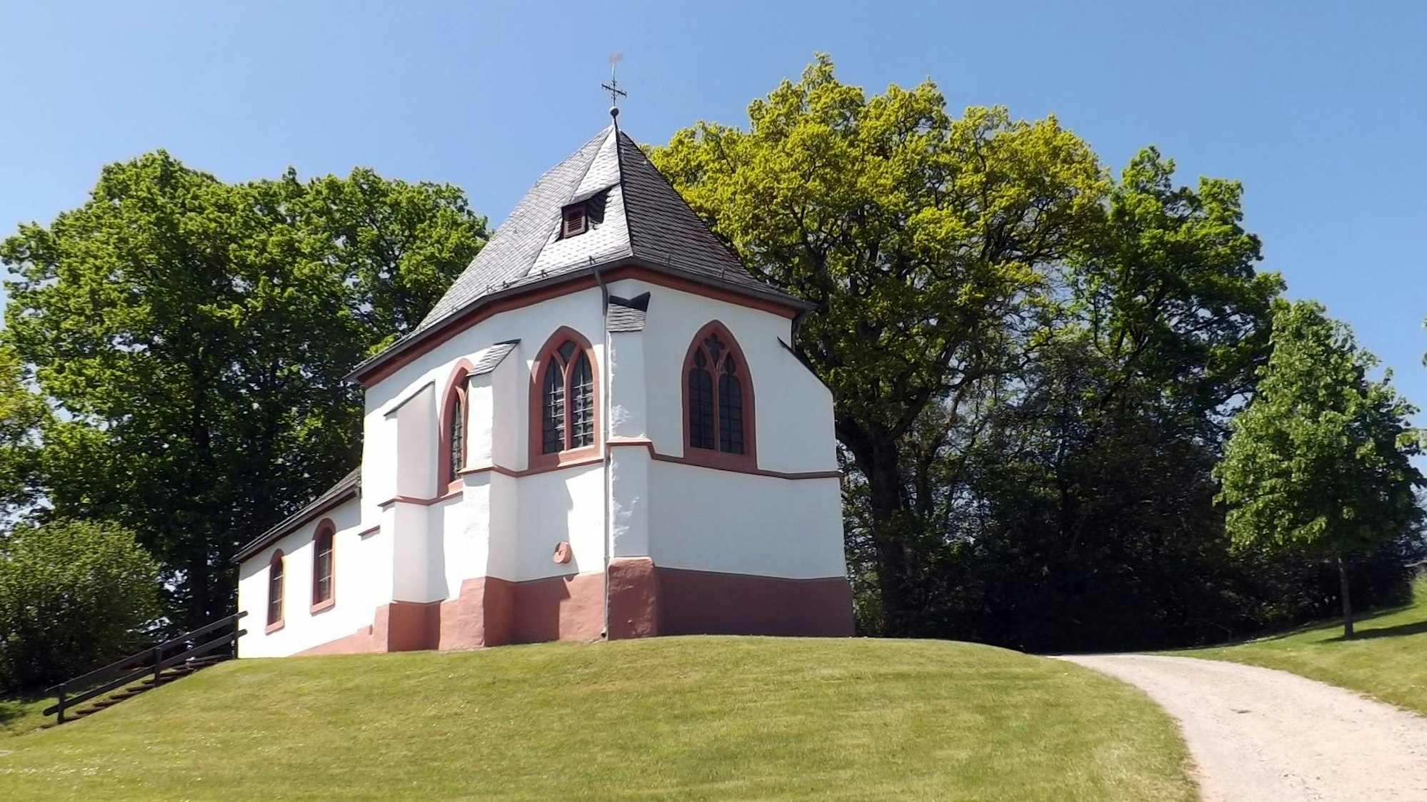 Die Ahekapelle mit weiß-rotem Anstrich vor grünen Bäumen