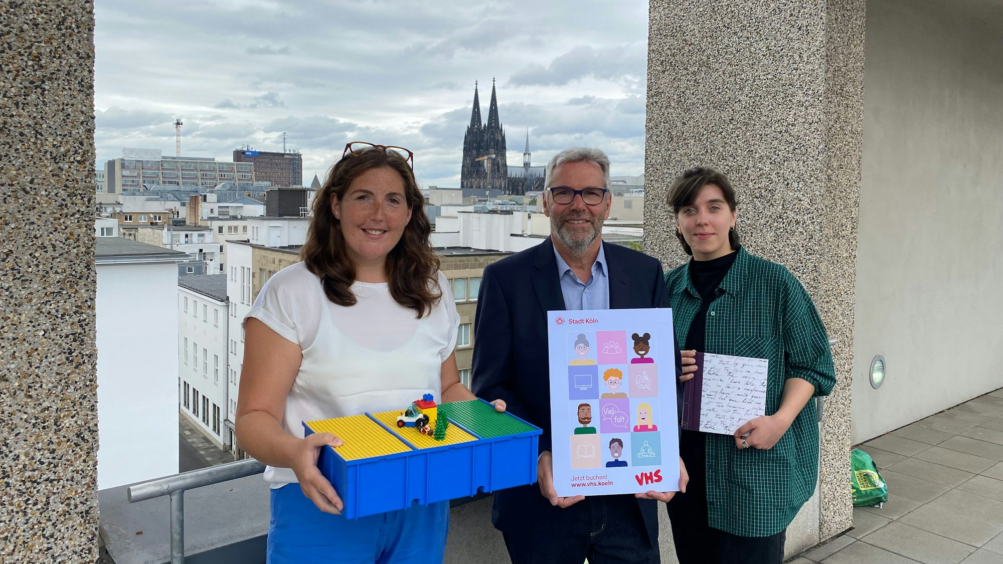 Auf dem Bild sieht man drei Leute auf einer Dachterrasse mit dem Kölner Dom im Hintergrund.