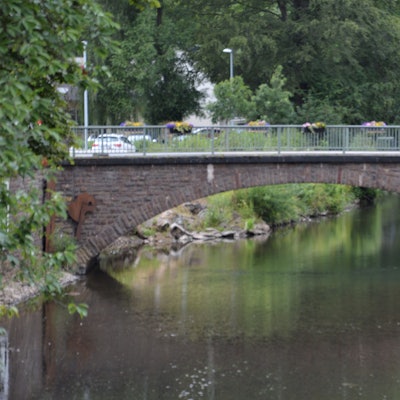 Zu sehen ist die beschädigte Brücke über die Olef in Schleiden. Am Geländer hängen Blumenkübel, links im Bild sind Bäume zu erkennen.